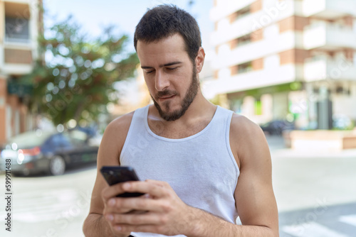 Young hispanic man using smartphone with relaxed expression at street