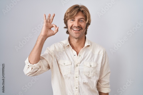 Middle age man standing over isolated background smiling positive doing ok sign with hand and fingers. successful expression.