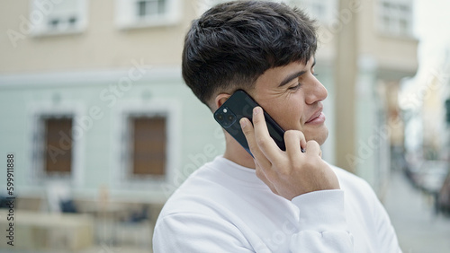 Young hispanic man talking on smartphone smiling at street