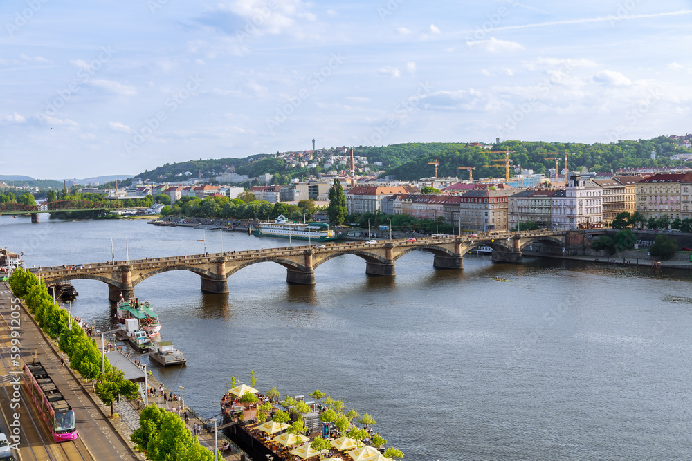 Fototapeta premium Top view of the stone transport bridge over the Vltava river, traffic of cars on the bridge, old architectural buildings. Beautiful summer landscape of the city of Prague.
