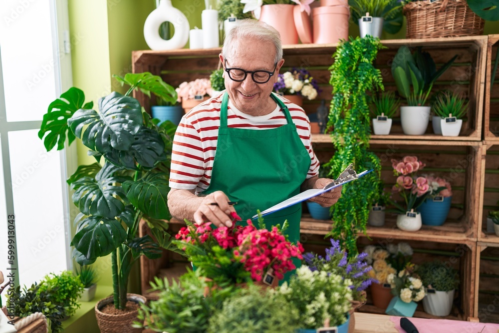 Middle age grey-haired man florist reading document touching plant at flower shop