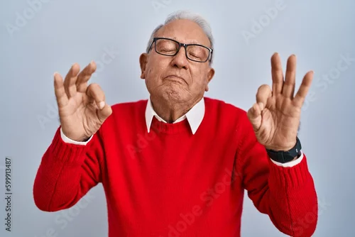 Obraz Senior man with grey hair standing over isolated background relaxed and smiling with eyes closed doing meditation gesture with fingers. yoga concept.