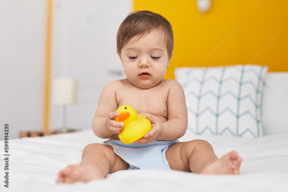 Adorable caucasian baby sitting on bed playing with duck toy at bedroom Adorable caucasian baby sitting on bed playing with duck toy at bedroom