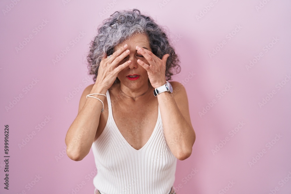 Middle age woman with grey hair standing over pink background rubbing eyes for fatigue and headache, sleepy and tired expression. vision problem Middle age woman with grey hair standing over pink background rubbing eyes for fatigue and headache, sleepy and tired expression. vision problem