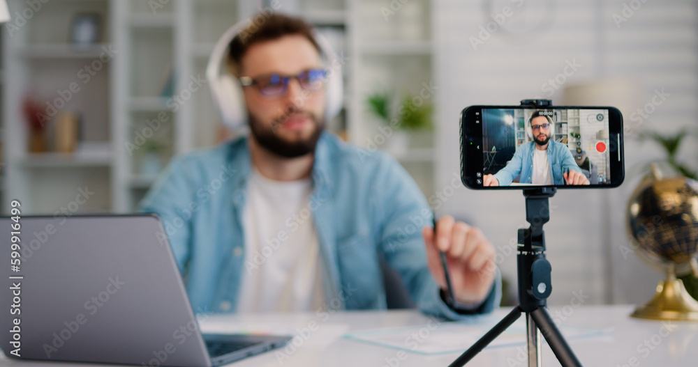 Focus on screen of smartphone. Young man is live streaming a training blog at home. Blogger using a smartphone while sitting at home in the kitchen with a laptop. Focus on screen of smartphone. Young man is live streaming a training blog at home. Blogger using a smartphone while sitting at home in the kitchen with a laptop.