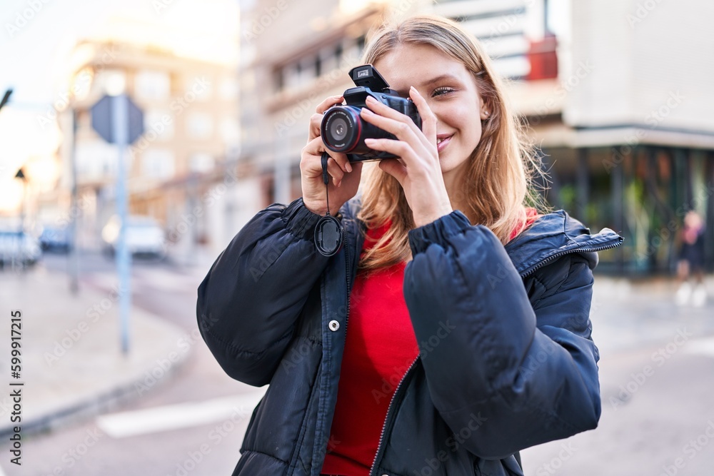 Young blonde woman smiling confident using professional camera at street