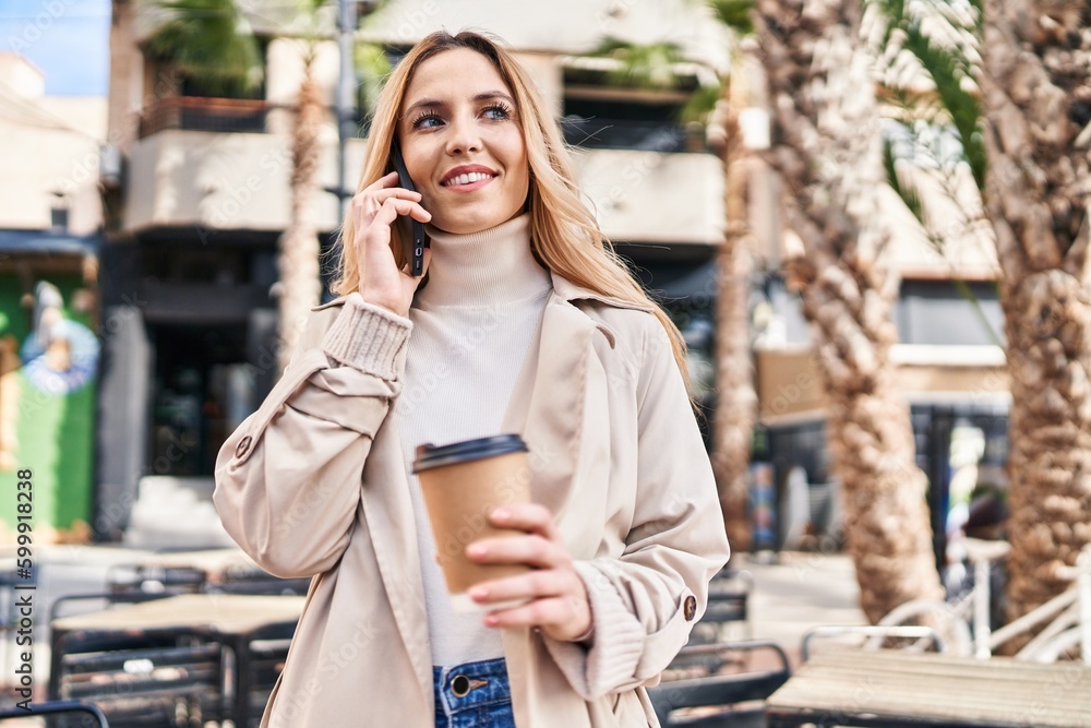 Fototapeta premium Young blonde woman talking on smartphone drinking coffee at coffee shop terrace
