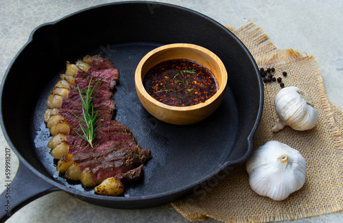 Medium rare steak in black pan with garlic rosemary and black peppers , Grilled picanha steak with spicy sauce in wooden bowl on burlap fabric