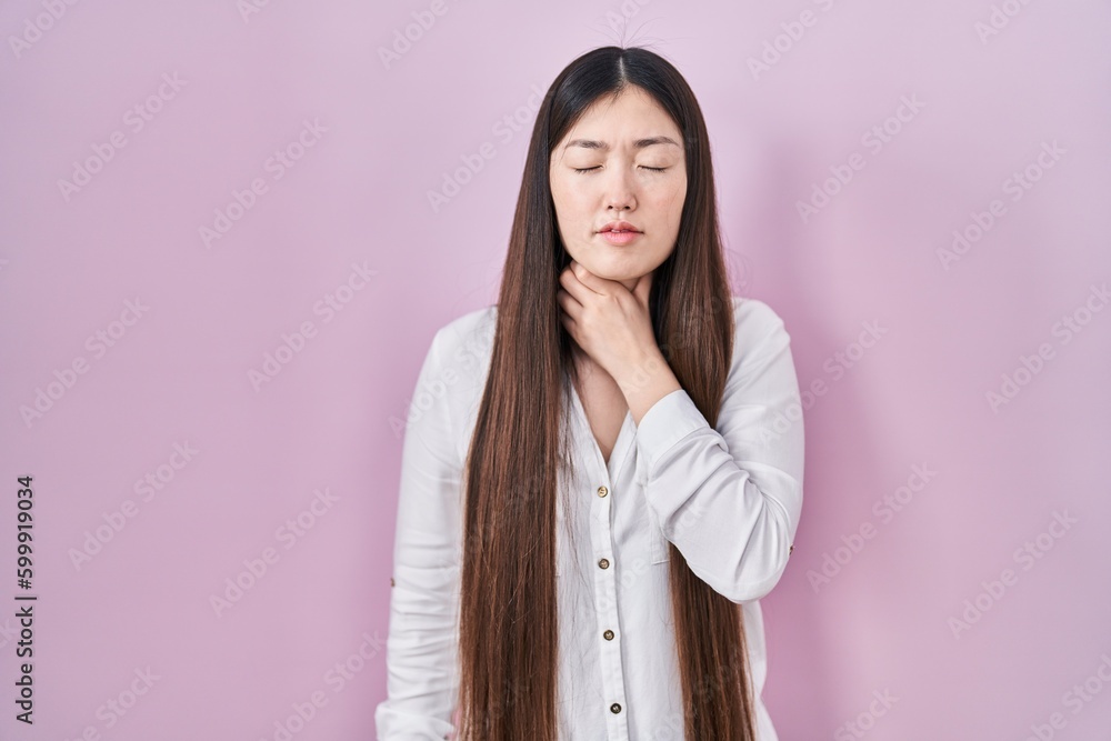 Fototapeta premium Chinese young woman standing over pink background touching painful neck, sore throat for flu, clod and infection