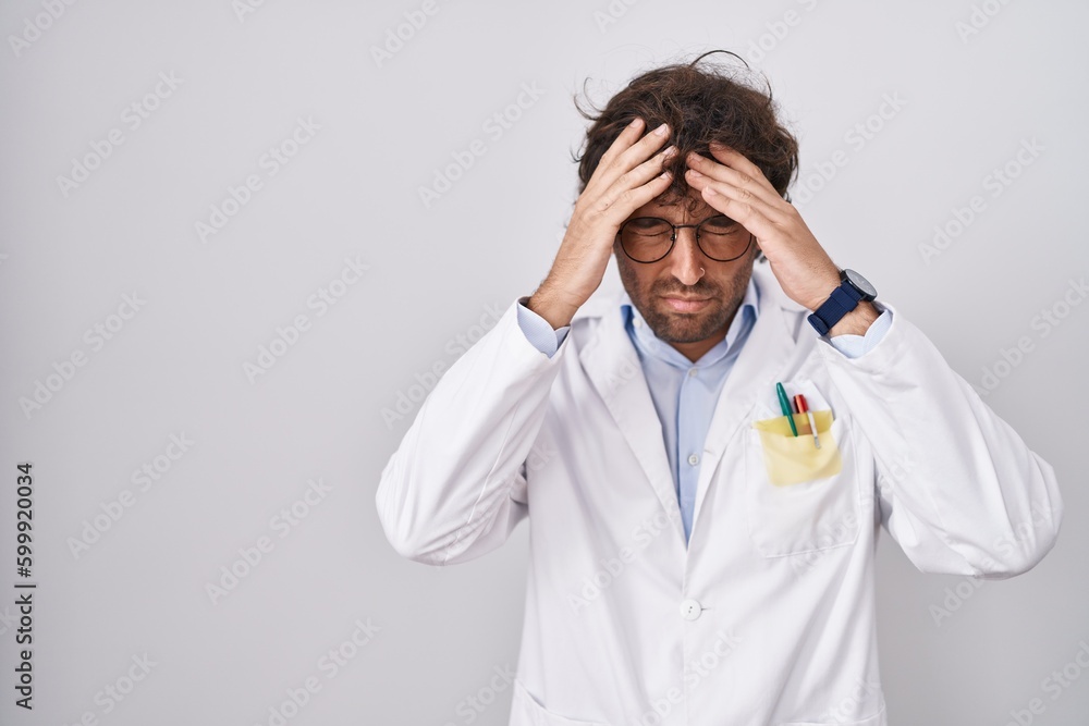 Hispanic young man wearing doctor uniform suffering from headache desperate and stressed because pain and migraine. hands on head. Hispanic young man wearing doctor uniform suffering from headache desperate and stressed because pain and migraine. hands on head.
