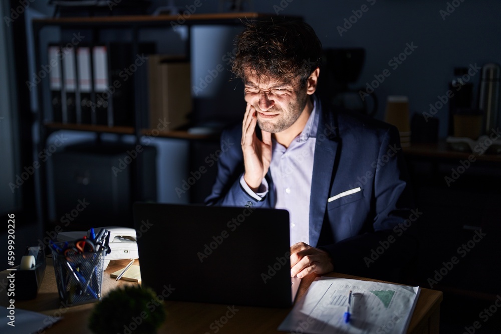 Hispanic young man working at the office at night touching mouth with hand with painful expression because of toothache or dental illness on teeth. dentist Hispanic young man working at the office at night touching mouth with hand with painful expression because of toothache or dental illness on teeth. dentist