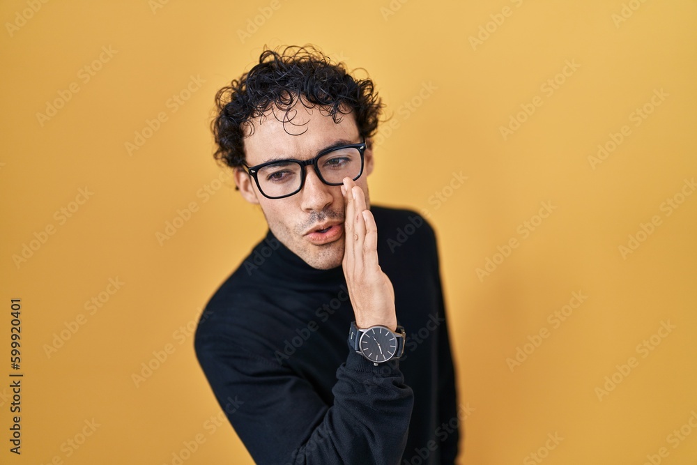 Hispanic man standing over yellow background hand on mouth telling secret rumor, whispering malicious talk conversation Hispanic man standing over yellow background hand on mouth telling secret rumor, whispering malicious talk conversation