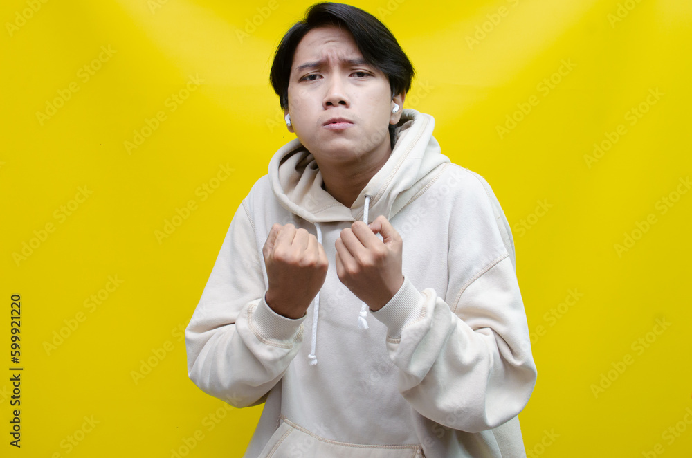 Obraz premium an Asian young man in beige hoodie, threatening, accusing, and looking for fight. A hysterical, mad depressed indonesian young man hand, shouts and screams loudly.