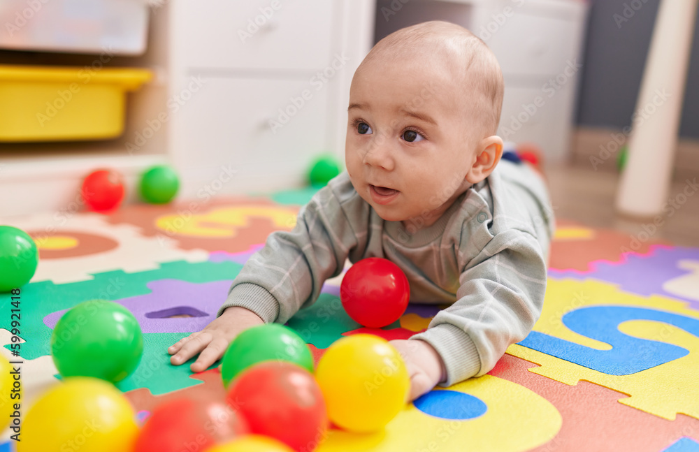 Adorable caucasian baby playing with balls lying on floor at kindergarten Adorable caucasian baby playing with balls lying on floor at kindergarten
