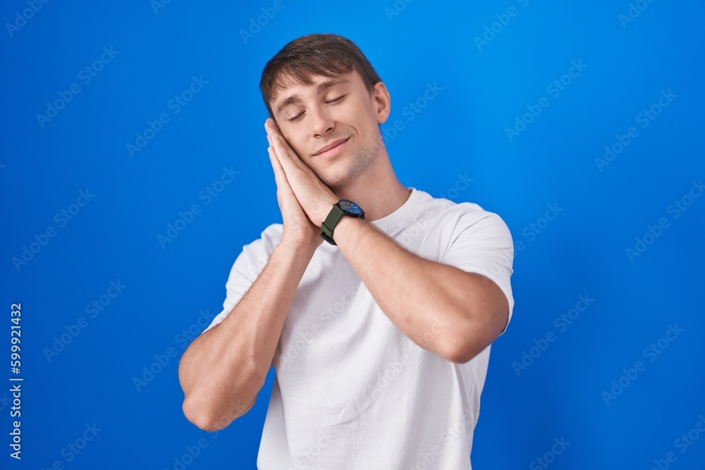 Caucasian blond man standing over blue background sleeping tired dreaming and posing with hands together while smiling with closed eyes. Caucasian blond man standing over blue background sleeping tired dreaming and posing with hands together while smiling with closed eyes.