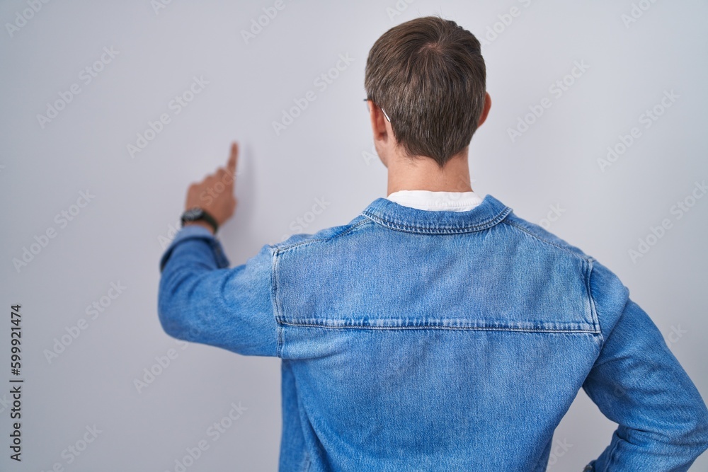 Caucasian blond man standing wearing glasses posing backwards pointing ahead with finger hand Caucasian blond man standing wearing glasses posing backwards pointing ahead with finger hand