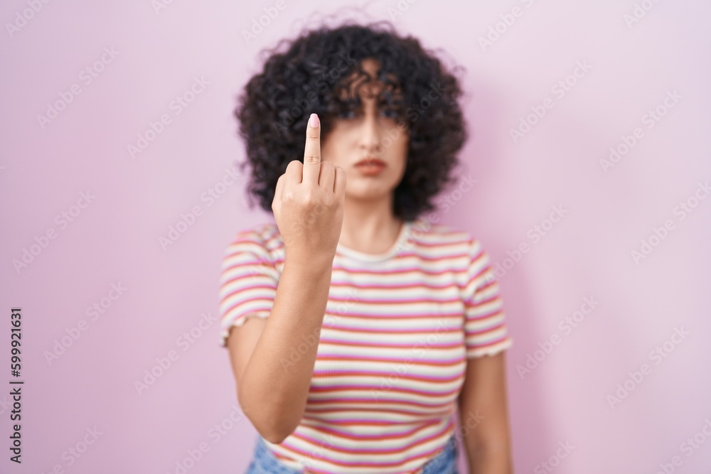 Young middle east woman standing over pink background showing middle finger, impolite and rude fuck off expression Young middle east woman standing over pink background showing middle finger, impolite and rude fuck off expression