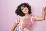 Young middle east woman standing over pink background dancing happy and cheerful, smiling moving casual and confident listening to music