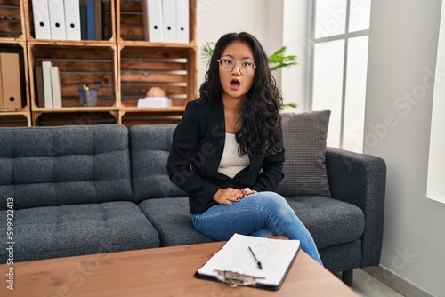 Young asian woman at consultation office afraid and shocked with surprise and amazed expression, fear and excited face.