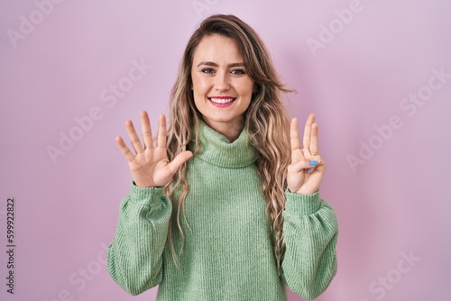 Young caucasian woman standing over pink background showing and pointing up with fingers number eight while smiling confident and happy.