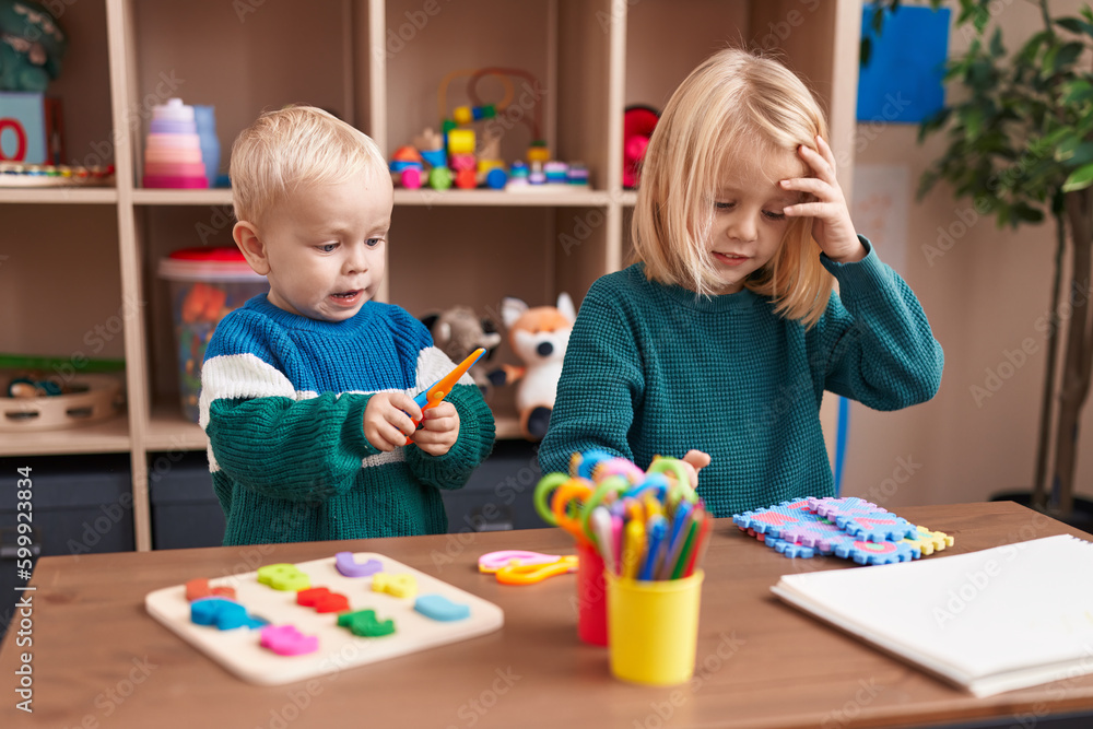 Fototapeta premium Adorable boy and girl playing with maths puzzle game holding scissors at kindergarten