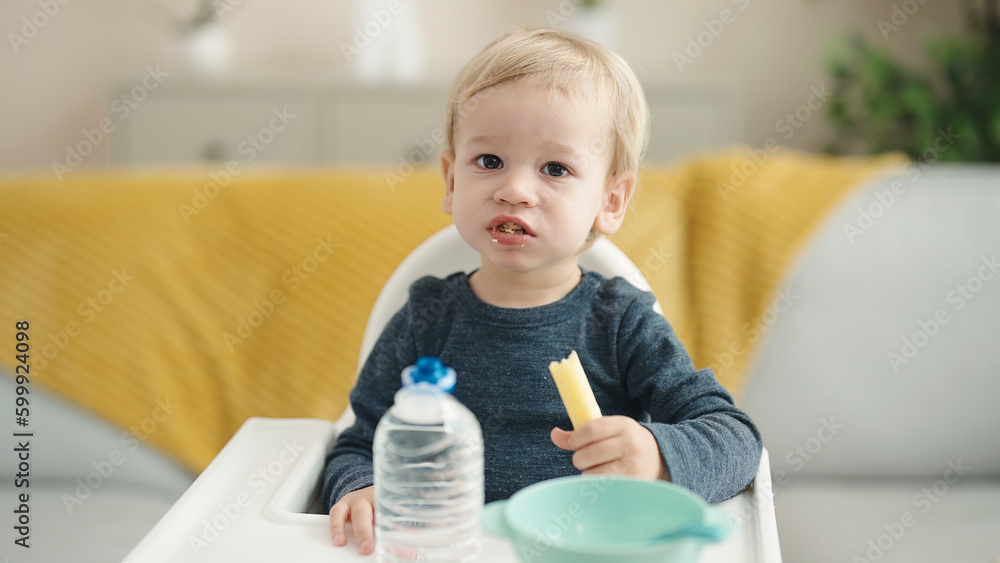 Adorable blond toddler sitting on highchair eating snack at home Adorable blond toddler sitting on highchair eating snack at home