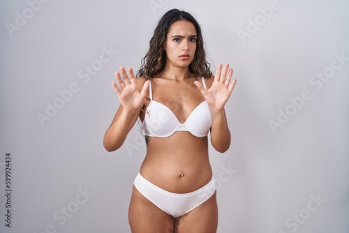 Young hispanic woman wearing white lingerie moving away hands palms showing refusal and denial with afraid and disgusting expression. stop and forbidden. © Krakenimages.com