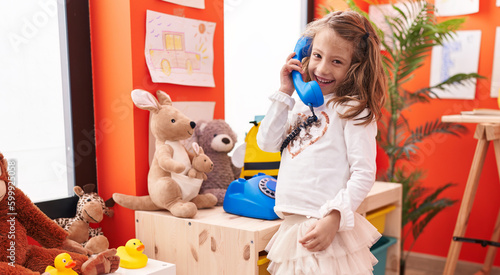 Adorable hispanic girl playing telephone toy standing at kindergarten photo