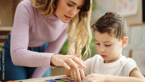 Woman and boy playing with maths puzzle game sitting on table at kindergarten