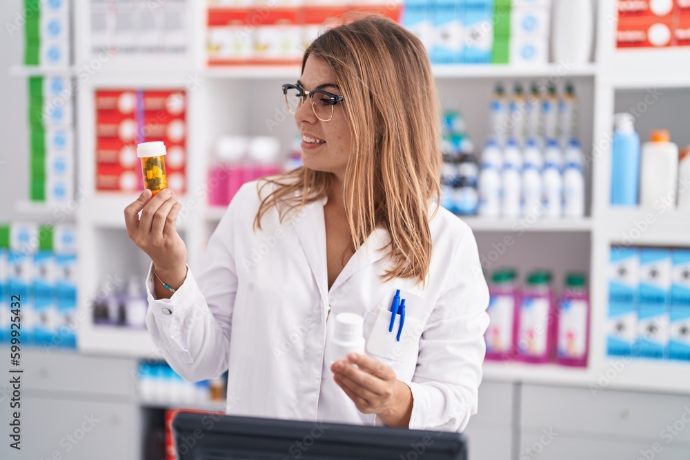 Young woman pharmacist smiling confident holding pills bottles at pharmacy