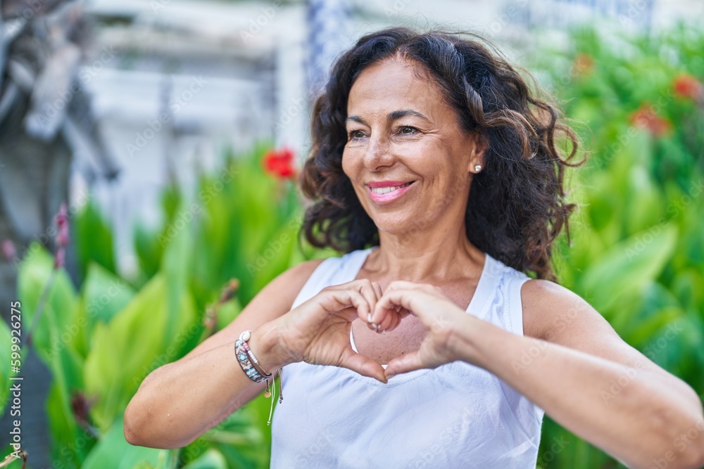 Middle age woman smiling confident doing heart gesture with hands at park Middle age woman smiling confident doing heart gesture with hands at park