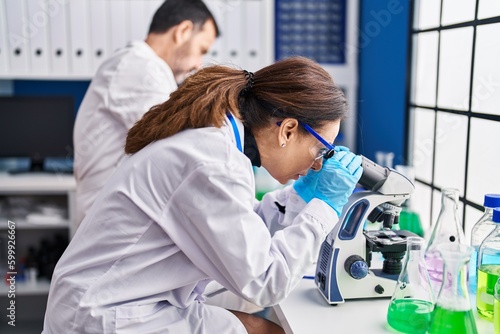 Middle age man and woman scientists using microscope working at laboratory