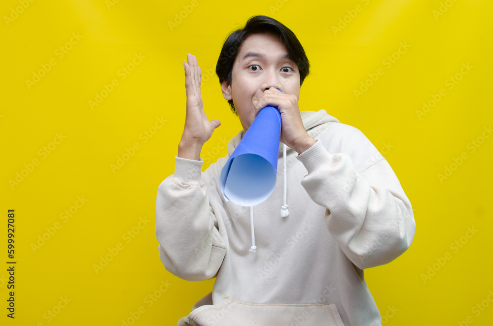 Shocked and surprised asian man shouting through paper megaphone giving an announcement. Shocked and surprised asian man shouting through paper megaphone giving an announcement.