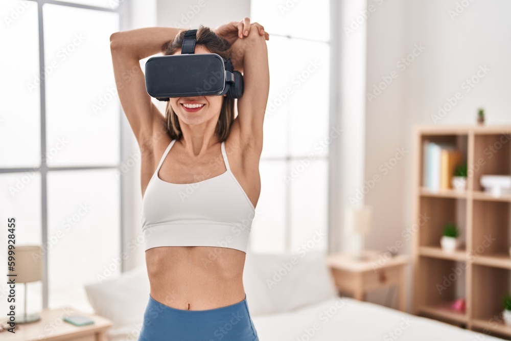 Young beautiful hispanic woman stretching arms using virtual reality glasses at bedroom