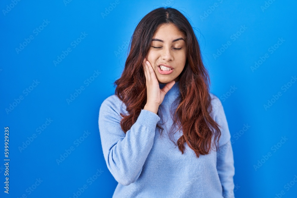 Hispanic young woman standing over blue background touching mouth with hand with painful expression because of toothache or dental illness on teeth. dentist Hispanic young woman standing over blue background touching mouth with hand with painful expression because of toothache or dental illness on teeth. dentist