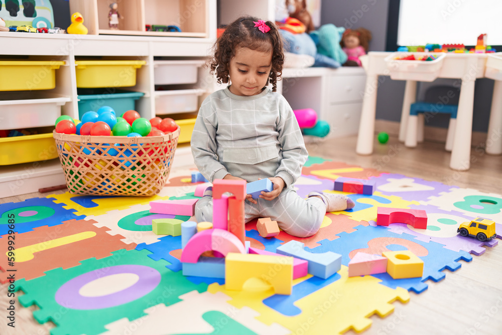 Fototapeta premium Adorable hispanic girl playing with construction blocks sitting on floor at kindergarten