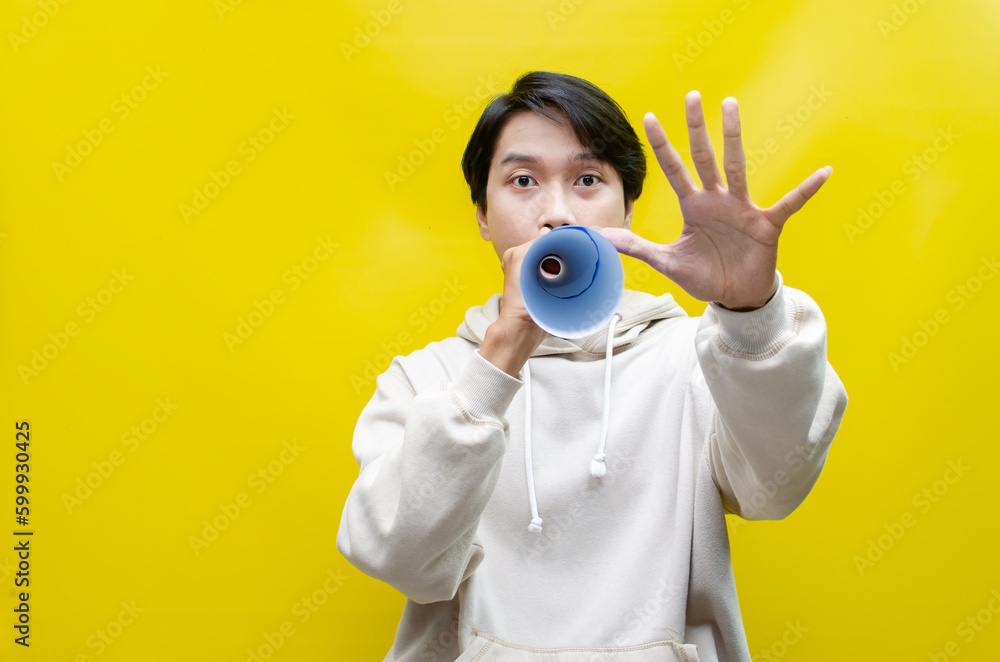 Shocked and surprised asian man shouting through paper megaphone giving an announcement.