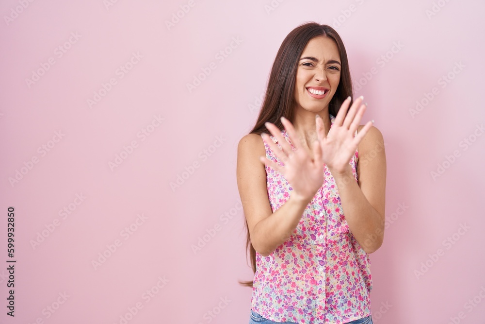 Young hispanic woman with long hair standing over pink background disgusted expression, displeased and fearful doing disgust face because aversion reaction. with hands raised Young hispanic woman with long hair standing over pink background disgusted expression, displeased and fearful doing disgust face because aversion reaction. with hands raised