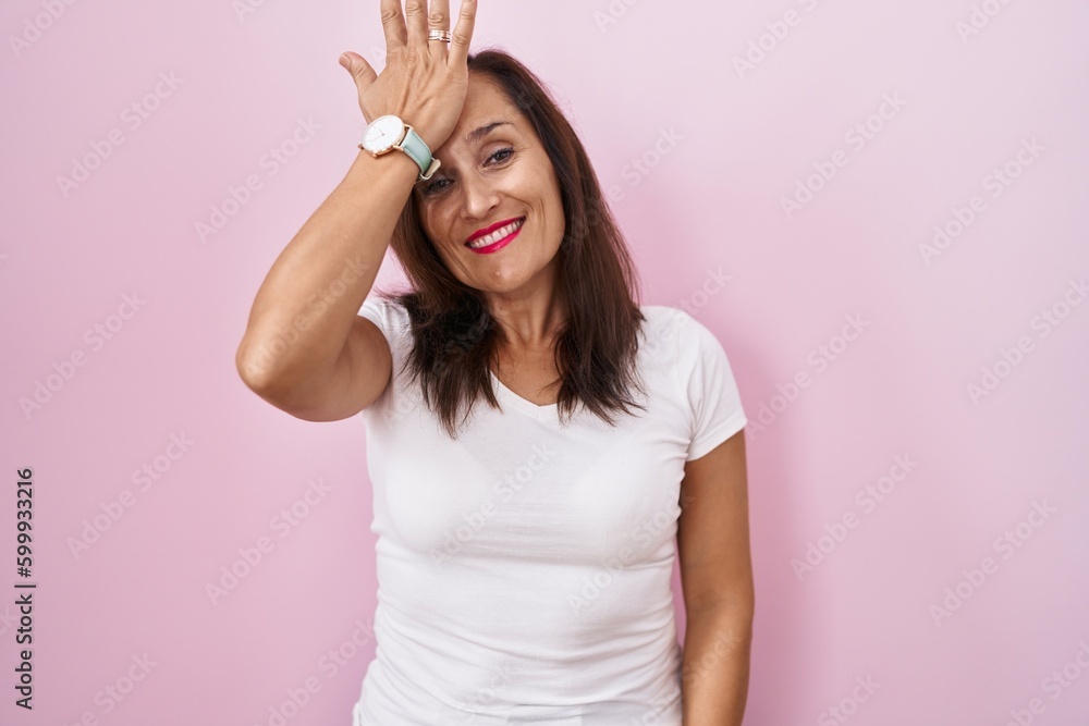 Middle age brunette woman standing over pink background surprised with hand on head for mistake, remember error. forgot, bad memory concept. Middle age brunette woman standing over pink background surprised with hand on head for mistake, remember error. forgot, bad memory concept.