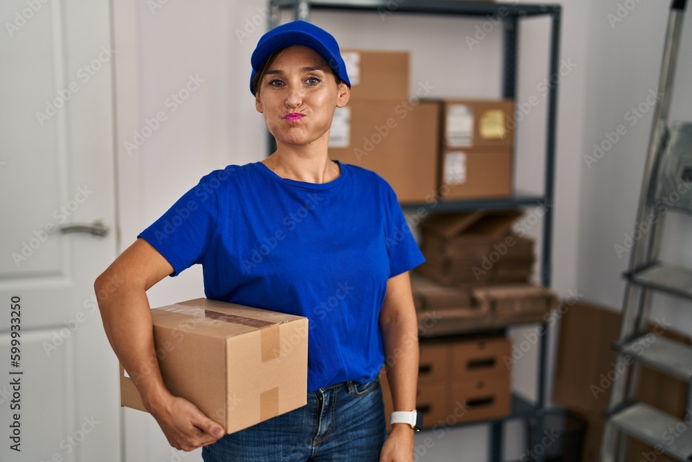 Middle age brunette woman working wearing delivery uniform and cap puffing cheeks with funny face. mouth inflated with air, crazy expression. Middle age brunette woman working wearing delivery uniform and cap puffing cheeks with funny face. mouth inflated with air, crazy expression.