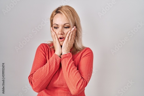 Blonde woman standing over isolated background tired hands covering face, depression and sadness, upset and irritated for problem