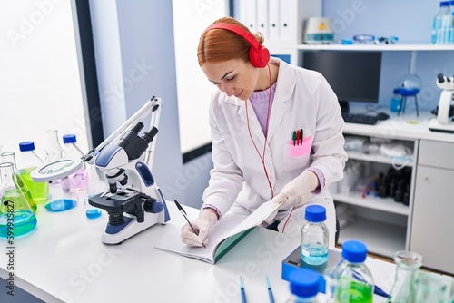 Young caucasian woman scientist listening to music writing on notebook at laboratory