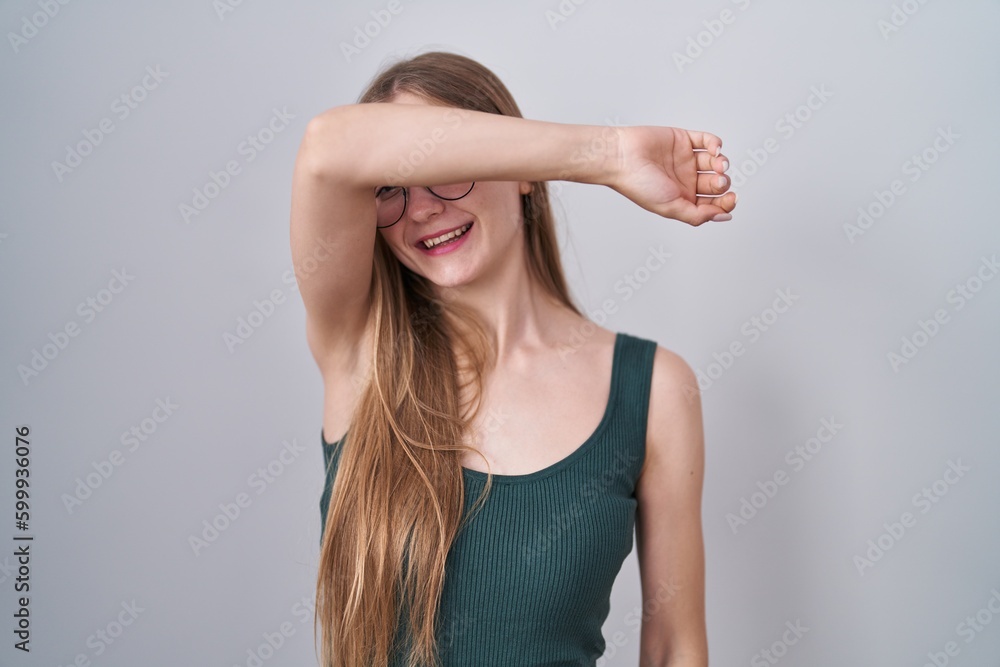 Young caucasian woman standing over white background covering eyes with arm smiling cheerful and funny. blind concept. Young caucasian woman standing over white background covering eyes with arm smiling cheerful and funny. blind concept.