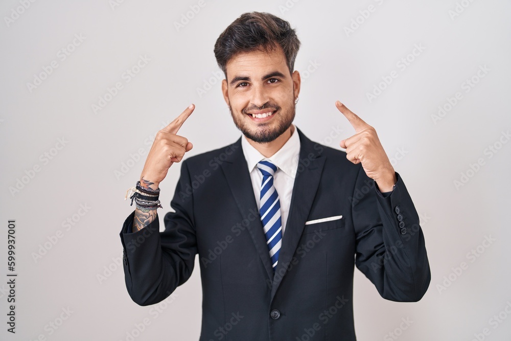 Young hispanic man with tattoos wearing business suit and tie smiling pointing to head with both hands finger, great idea or thought, good memory Young hispanic man with tattoos wearing business suit and tie smiling pointing to head with both hands finger, great idea or thought, good memory