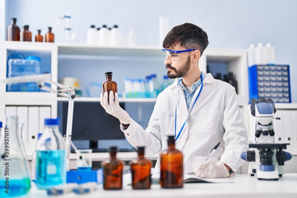 Young hispanic man scientist writing on notebook holding bottle at laboratory Young hispanic man scientist writing on notebook holding bottle at laboratory