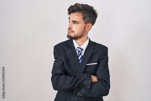 Young hispanic man with tattoos wearing business suit and tie looking to the side with arms crossed convinced and confident