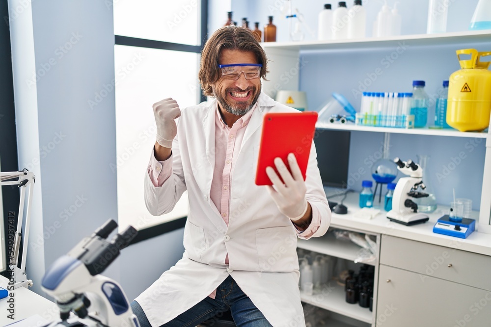 Handsome middle age man working at scientist laboratory doing video call screaming proud, celebrating victory and success very excited with raised arm Handsome middle age man working at scientist laboratory doing video call screaming proud, celebrating victory and success very excited with raised arm