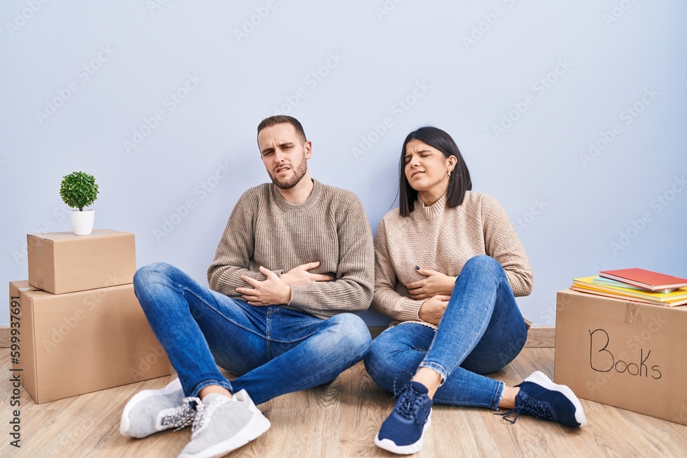 Young couple moving to a new home with hand on stomach because indigestion, painful illness feeling unwell. ache concept. Young couple moving to a new home with hand on stomach because indigestion, painful illness feeling unwell. ache concept.