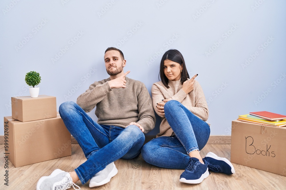 Young couple moving to a new home pointing with hand finger to the side showing advertisement, serious and calm face Young couple moving to a new home pointing with hand finger to the side showing advertisement, serious and calm face
