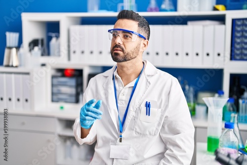 Young hispanic man scientist speaking at laboratory
